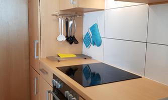 A modern kitchen with wooden cabinets and a cooking stove. Cooking utensils and a pot holder hang on the wall.