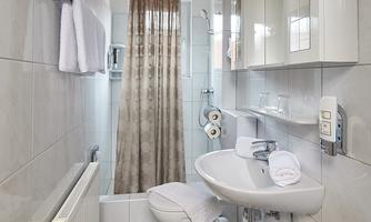 A modern bathroom with gray tiles and a shower curtain. It includes a sink, a toilet, and towels.