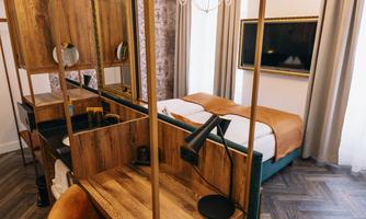A modern hotel room with a cozy bed and wooden furniture. The room has an elegant desk and a television on the wall.