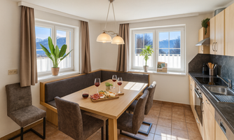 A bright kitchen with a dining table surrounded by comfortable chairs. Through the windows, a beautiful view of the mountains and nature can be seen.