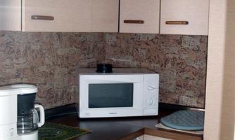 A modern kitchen with light cabinets and a small table. A microwave and a coffee machine are visible on the countertop.