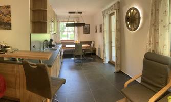 A modern kitchen and dining area with wooden furniture and a large window. The space is bright and inviting, ideal for social gatherings.