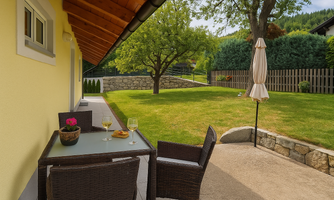 A cozy terrace with a table and chairs, surrounded by a well-maintained garden. In the background stands a tree and a sunny meadow invites you to relax.