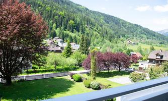 A beautiful landscape with green meadows and colorful trees. In the background, gentle hills and small houses can be seen.