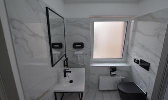 A modern bathroom with marble walls. There is a sink, a mirror, and a window that lets in natural light.
