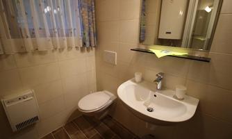 A small, modern bathroom with a sink, a toilet, and a mirror. The walls are tiled in light colors, and there are two cups on the sink.