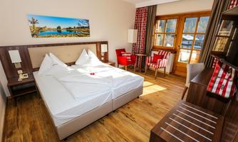 A cozy hotel room with a large double bed and modern furniture. Large windows offer a view of nature and let in plenty of light.