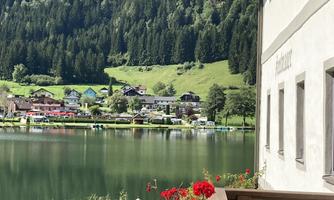 A picturesque landscape with a clear lake and green mountains in the background. In the foreground, there are colorful flowers on a balcony.