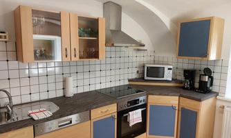 A modern kitchen with wooden and blue cabinets. It includes cooking appliances, a microwave, and a sink.
