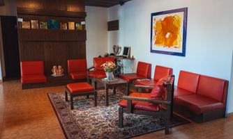 A cozy waiting area with red furniture and a colorful painting on the wall. The room is bright and inviting, ideal for relaxed encounters.