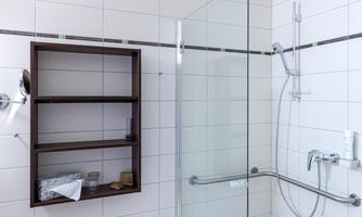 A modern bathroom with a glass shower and white tiles. A shelf for toiletries is mounted on the wall.
