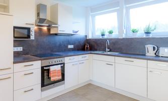 Modern, bright kitchen with white cabinets and dark countertops. Windows with plants create a friendly atmosphere.