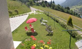 A beautiful garden with sun loungers and a parasol. In the background, mountains and a green meadow can be seen.