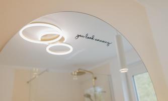 A round mirror with modern light rings. It features the cursive text "you look amazing".