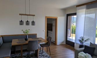 A bright and modern living-dining room with a table, chairs, and a cozy seating area. Large windows offer a view of the outdoors and provide plenty of natural light.