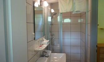 A modern bathroom with a shower, sink, and mirror. The walls are tiled, and there are towels on the shower.