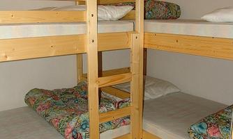 A room with two wooden bunk beds. The bedspreads are colorful and the mattresses are uncovered.