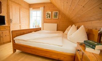 A cozy bedroom with wood paneling and a double bed. There is a wardrobe, a television, and a window with curtains.