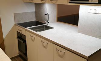 A modern kitchen with white cabinets and a gray countertop. It is equipped with a sink, a stove, and a microwave oven.