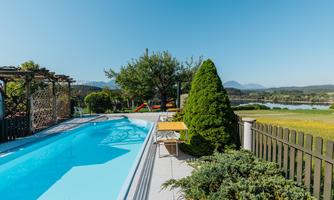 A beautiful pool in a sunny setting with trees and a green lawn in the background. Gentle hills are visible in the background.