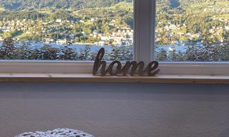 A cozy room with a view of gentle hills and a city in the background. A wooden sign reading "home" stands in the foreground.