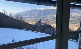 A view of a castle in the distance, surrounded by snow and mountains. The sight is framed like a window.