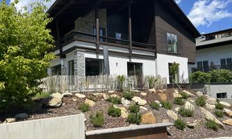 A modern house with a beautiful garden and stones. The sky is blue and the surroundings are bright and inviting.