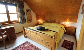 A cozy bedroom with wooden paneling and a large bed. There is a desk and a mirror on the wall.