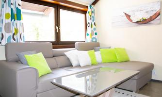 A modern living room with a bright couch and colorful cushions. Large windows let in a lot of light, and the decorative curtains enhance the friendly atmosphere.