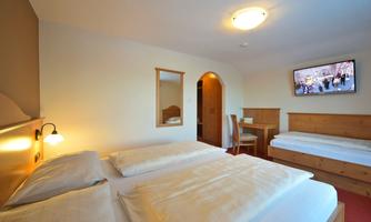 A cozy hotel room with a double bed and a single bed. It features a television and warm lighting.