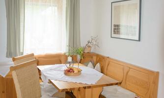 A cozy dining area with a wooden table and a corner bench. The rooms are bright and friendly with large windows and soft colors.