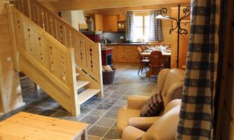 A cozy wooden house with an open living kitchen and a staircase. The space is bright and inviting, with a dining area and comfortable seating.