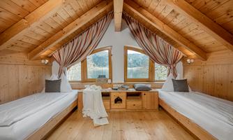 A cozy bedroom with wooden paneling and two single beds. Large windows offer a view of the nature outside.