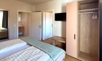 A modern room with two beds and light wooden flooring. The room includes a wardrobe and a television.