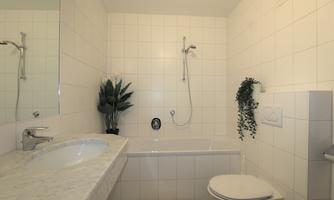 A modern bathroom with a bathtub and a shower. The room is bright with white tiles and a minimalist decor.