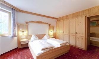 A cozy room with two beds and warm wooden paneling. Bright windows let in plenty of daylight.