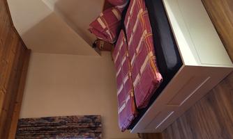 A cozy bedroom with a double bed and colorful cushions. The room features wooden details and a small window view outside.