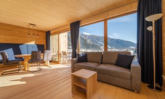 A bright and modern living room with large windows that offer a view of the mountains. The elegant furnishings include a cozy sofa and a wooden table.