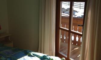 A cozy bedroom with a bed and colorful bedding. Through the window, you can see a balcony and snow-covered mountains.