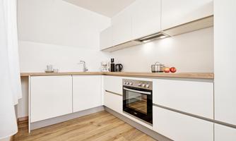 A modern kitchen with white cabinets and a wooden countertop. On the countertop, there is a kettle, a pot, and some apples.