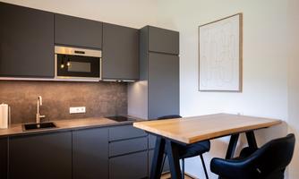 Modern kitchen with gray cabinets and stainless steel appliances. A stylish wooden dining table is located in the corner.