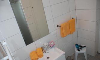A modern bathroom with white tiled walls. There is a sink, towels in yellow, and a mirror.