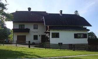 A large, two-story house with a beautiful garden and green lawn. The facade is white, and the windows have flower boxes.