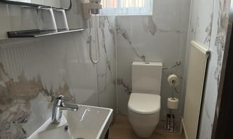 A modern bathroom with a sink, a toilet, and a large window. The walls are covered with stylish marble-like design.