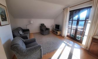 A bright living room with a large window and a beautiful view. There are comfortable armchairs and a television.