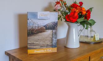 A stylish restaurant menu on a wooden table, next to a flower arrangement in a white vase. The background shows a cozy, inviting atmosphere.