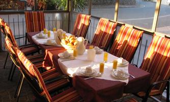 A set table in a light-filled room. On the table are breakfast items such as rolls, drinks, and crockery.