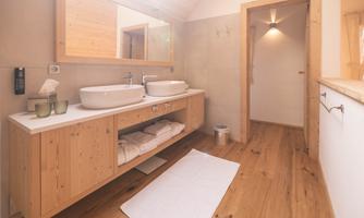 A modern bathroom with two sinks and a wooden cabinet. The floor is made of wood and there are fresh towels in sight.