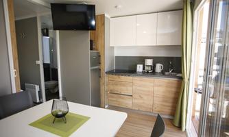 Modern kitchen with wooden cabinets and a bright dining area. A table with a green placemat and a decorative glass object is in the center.