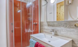 A modern bathroom with a shower cabin and a sink. The walls are light and the ceiling is made of wood, creating a cozy atmosphere.